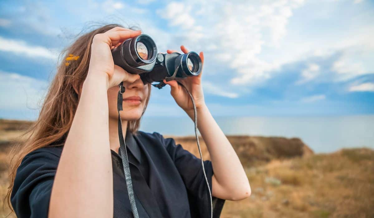 woman in her 30s looking through binoculars for adventure