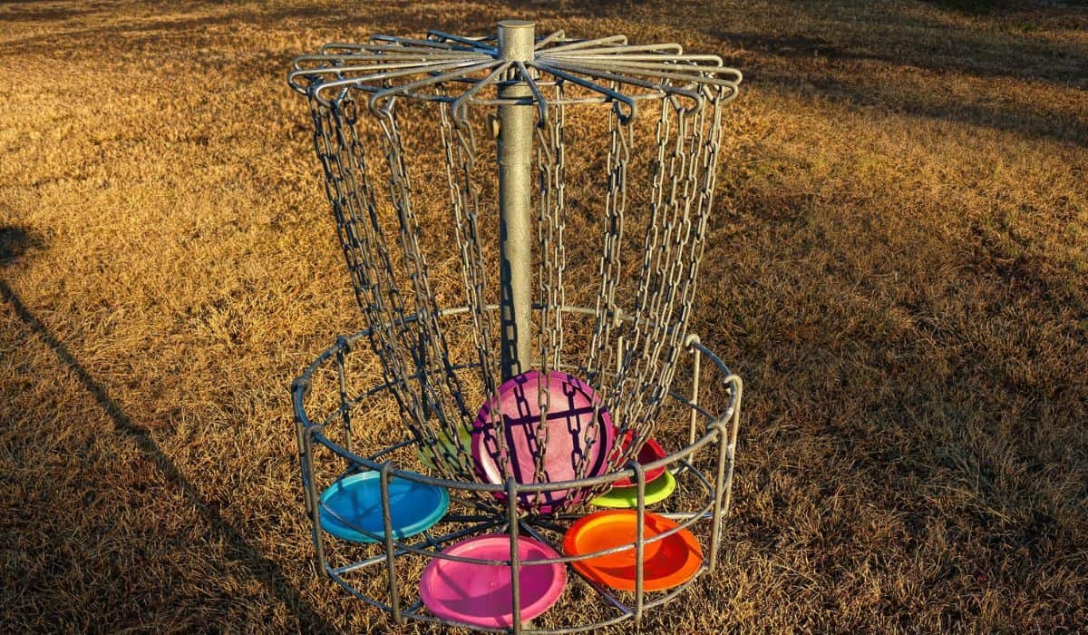 Disc golf basket with discs at sunset.