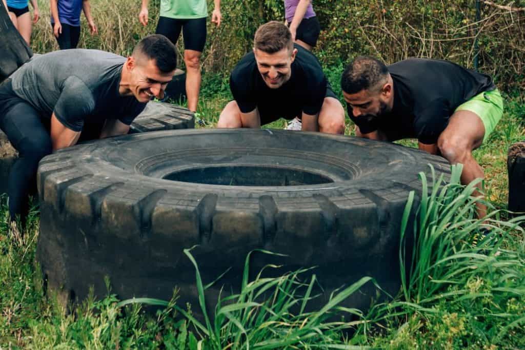 Three men helping each other to lift a huge tire