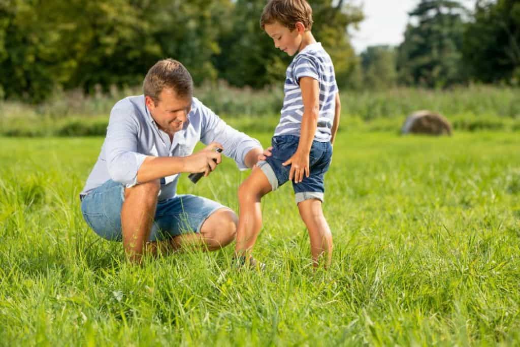 a father using bug spray on his son's leg outdoors