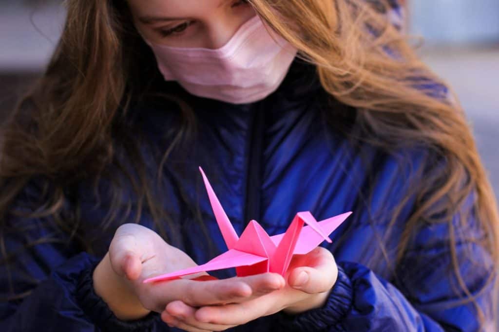 a teenage girl in mask doing origami