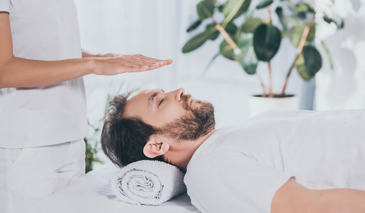 calm bearded man with closed eyes receiving reiki treatment above head