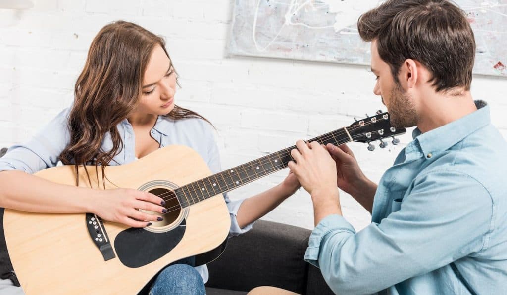 man teaching a woman to play the guitar