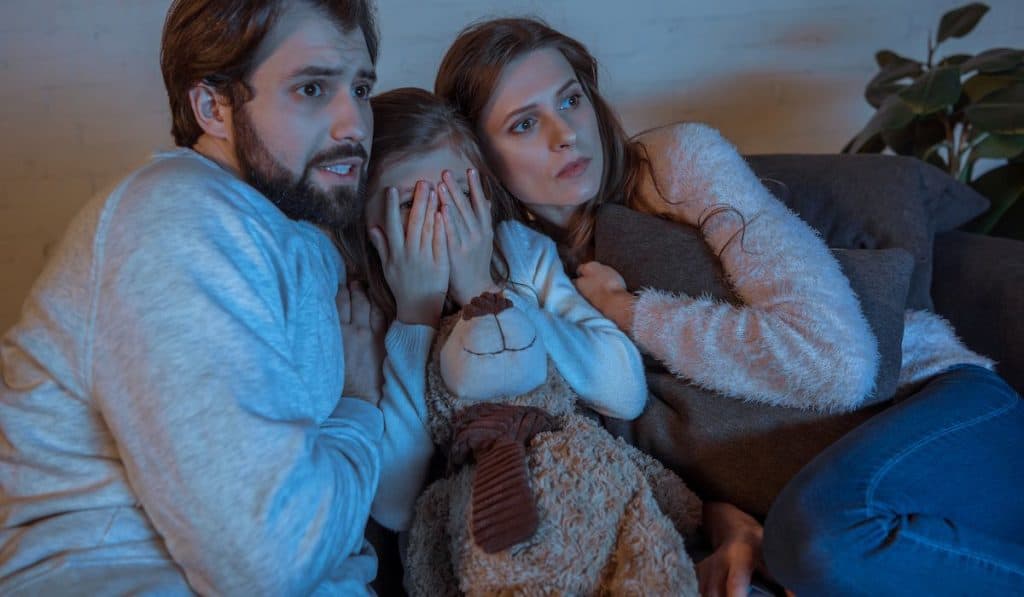parents watching a horror movie with their daughter