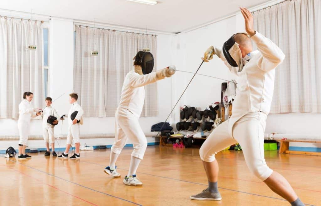 two men showing off their fencing skills in front of young fencers