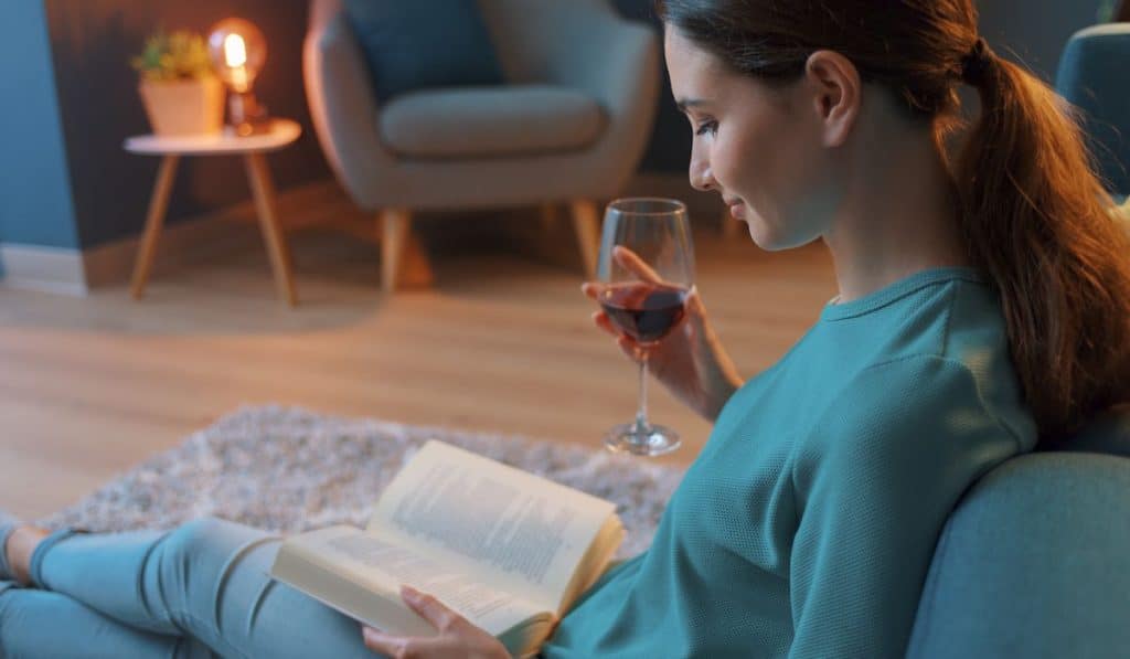 woman reading a book while holding a glass of red wine