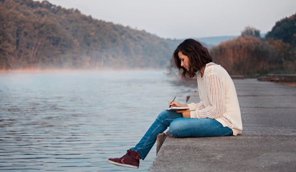 woman writing her diary at the side of a lake