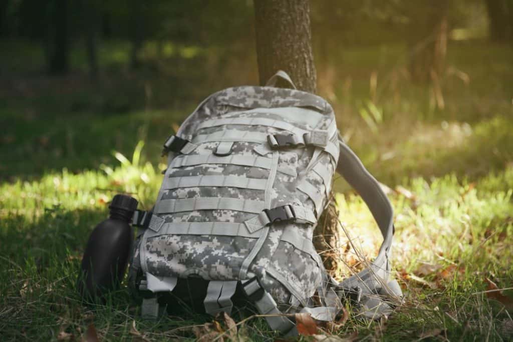 Military backpack with a canteen leaning on a tree trunk 