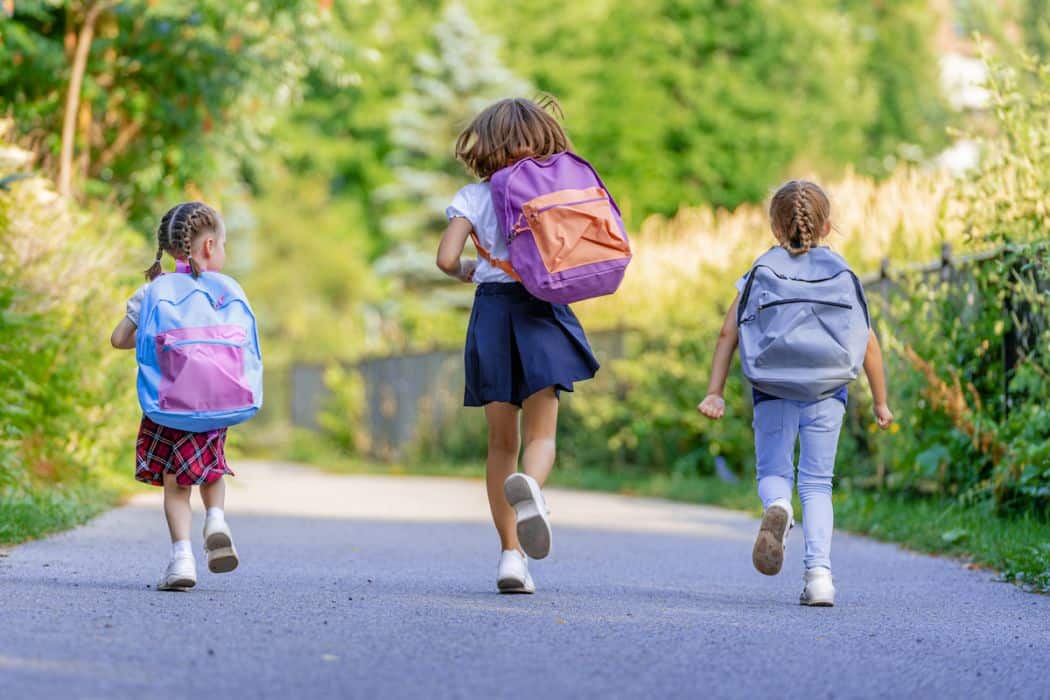 Three young girls running to go to school carrying their backpacks