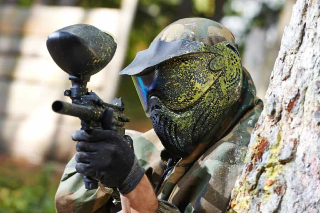 a man aiming a paintball gun with helmet tainted with yellow paint 