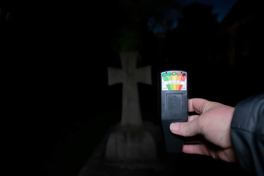 a man holding a ghost hunting instrument to detect ghost in a cemetery
