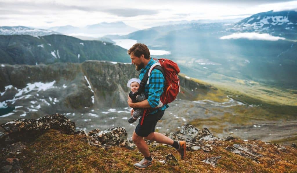 dad carrying his baby on a carrier near a cliff slope