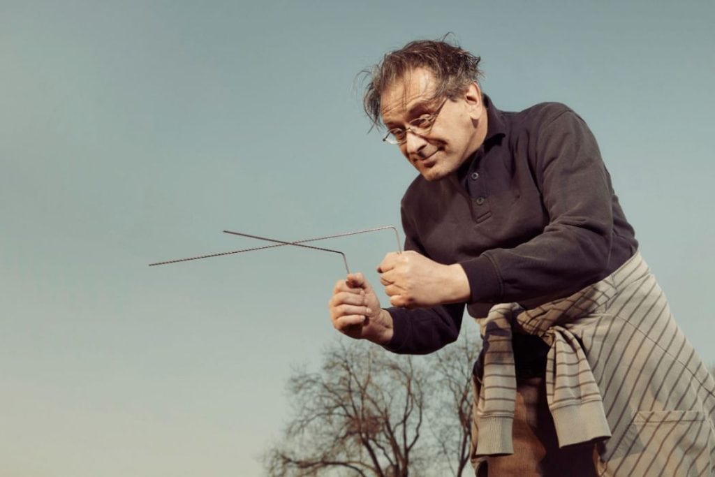 A man in black holding an L-shape rod practising dowsing