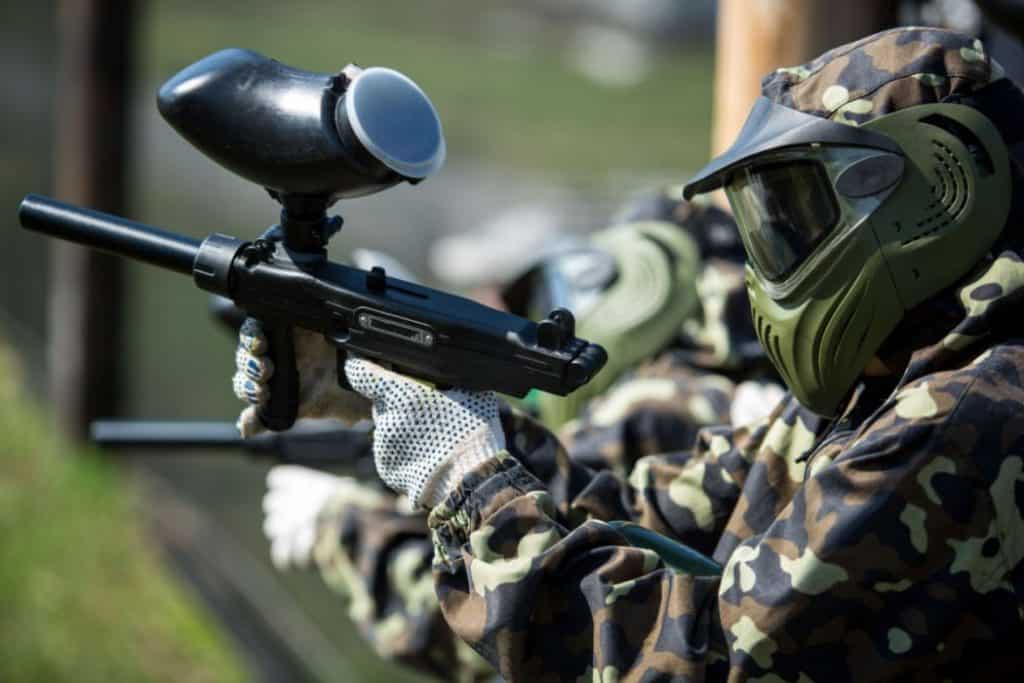 A man in full gear holding and aiming paintball gun 