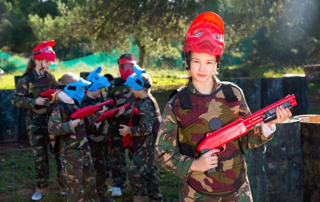 A young girl in red helmet holding a red paintball gun