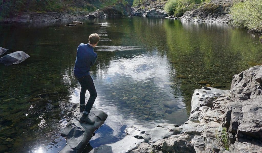 a young man stoneskipping near a water source