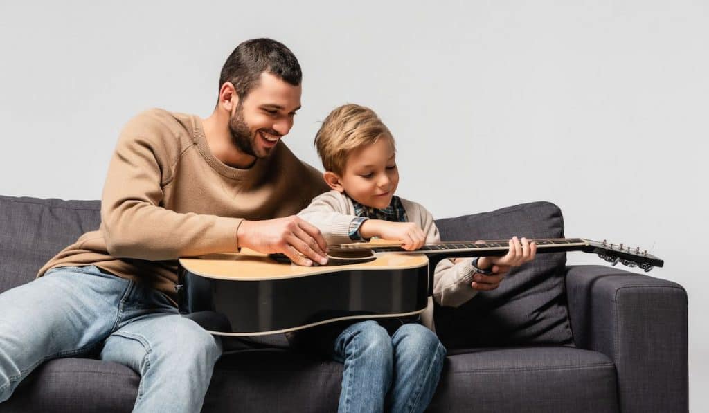 father happily teaching son to play the guitar