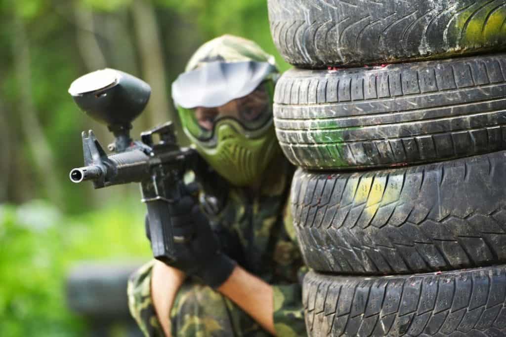 paintball player hiding beside piled up tires holding a paintball gun