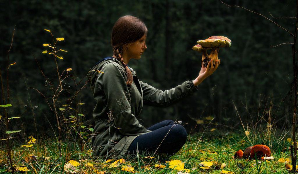 young woman holding and looking at a foraged mushroom