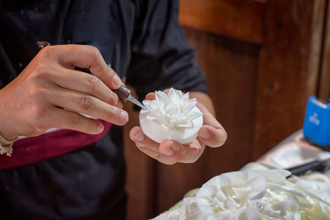 Young hand carving flowers from white soap