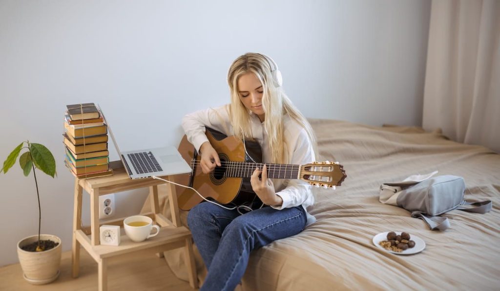 blonde girl learning to play guitar in her bedroom