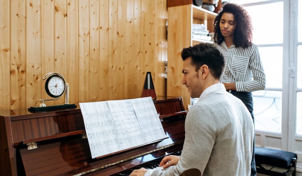 man teaching a woman to play the piano at home