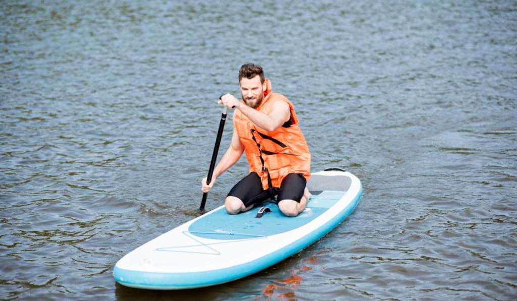 man on the paddleboard wearing an orange life jacket
