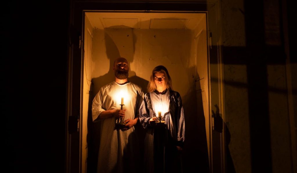 a couple in a dark room holding candles scaring people