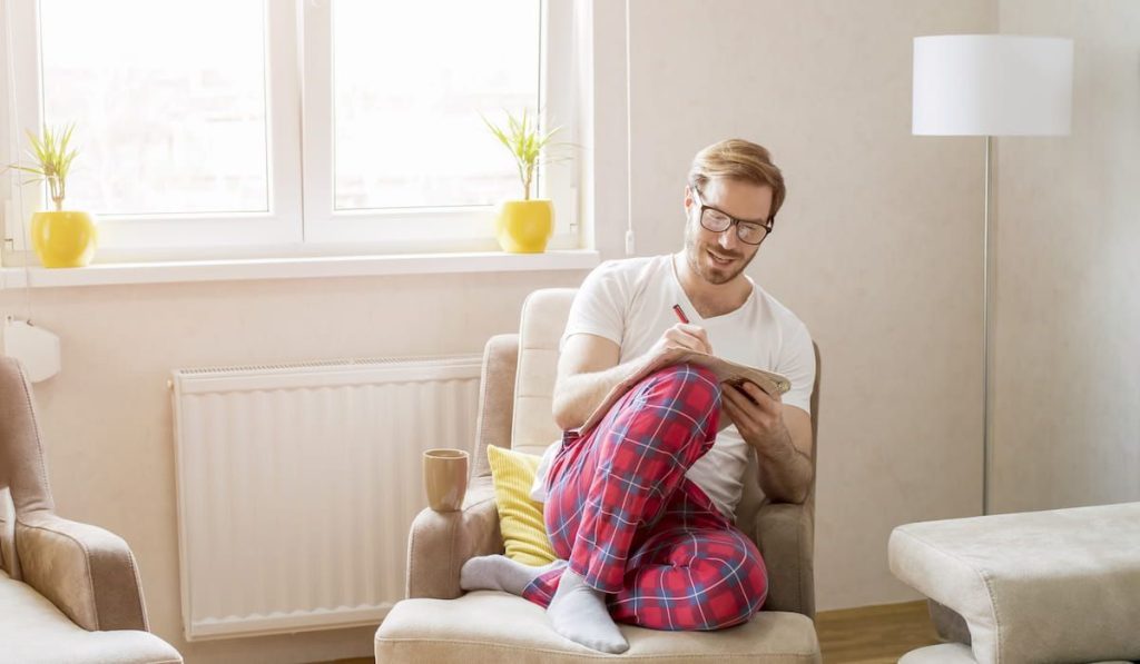 male sitting comfortably on the couch with a cup of coffee and a book of crossword puzzle