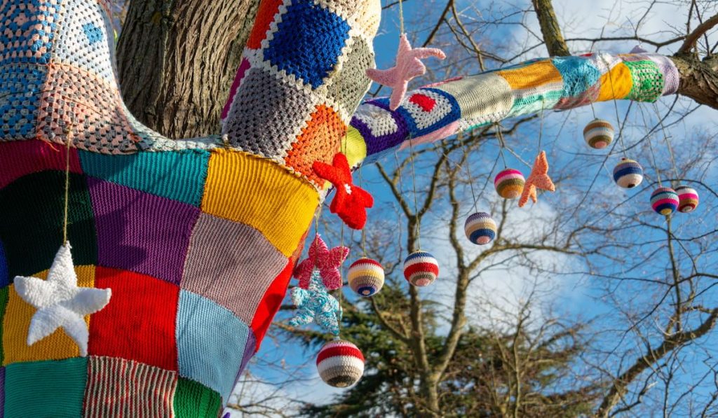 knitted and crochet yarn bombs hanging on a tree branch 