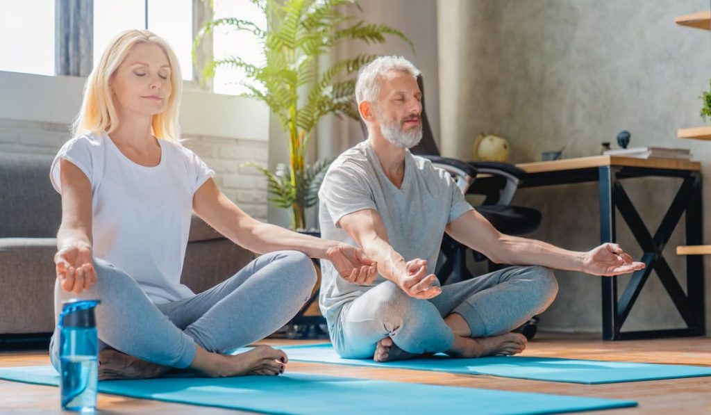 senior couple sitting on yoga mats meditating at home