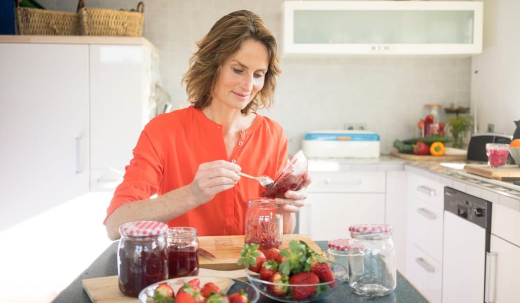 woman making strawberry jam, storing the finish product in a mason jar