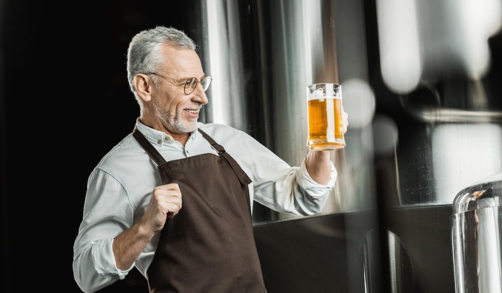 senior male brewer looking at glass of beer in brewery