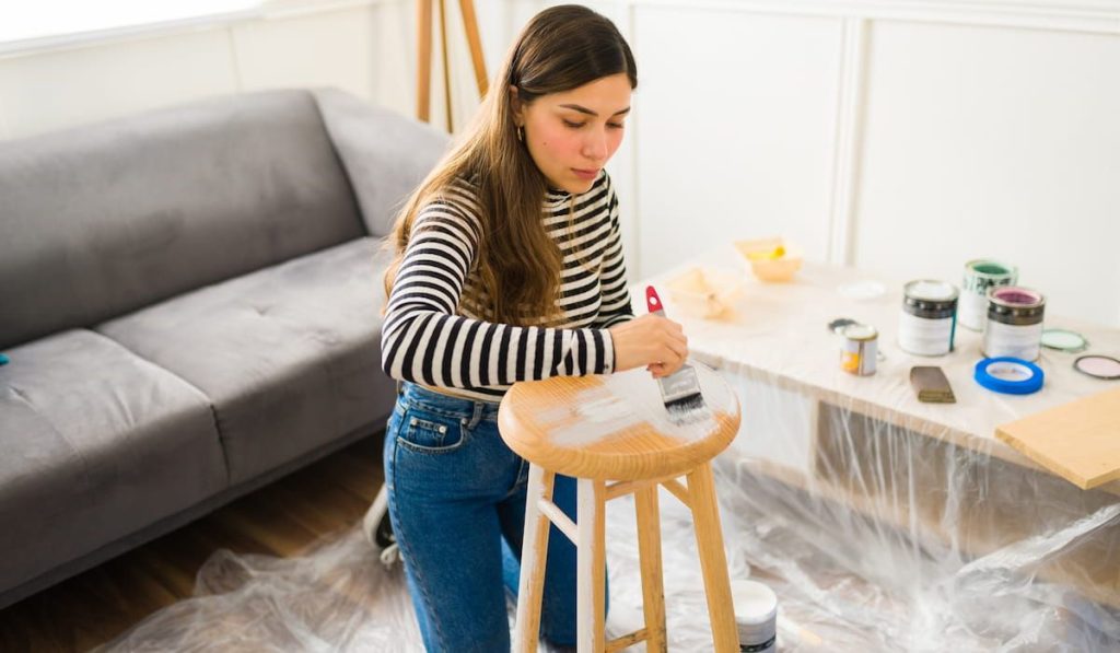 Beautiful young woman painting a stool on her DIY home improvement project or furniture flipping