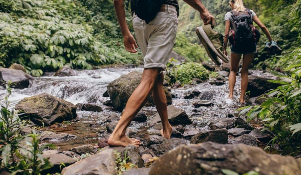 Hikers walking by the creek in forest with their shoes in hand