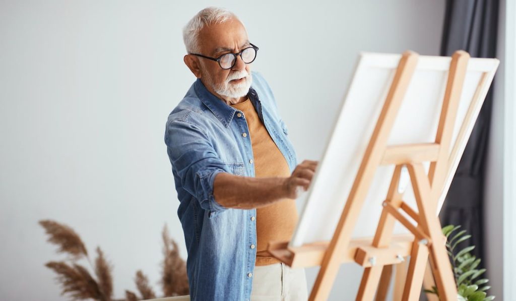 Senior painting on canvas at home studio.