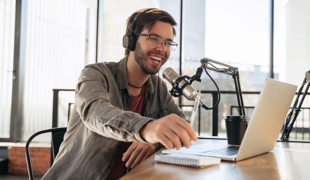 Young man host in headphones and glasses enjoying podcasting in studio