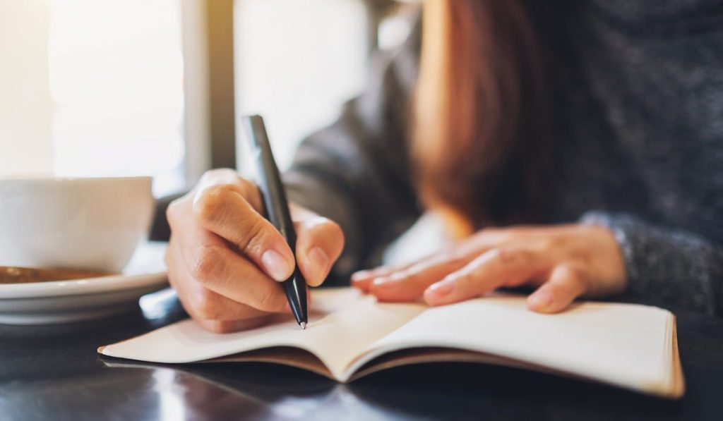 Closeup image of a woman writing on a notebook on the table