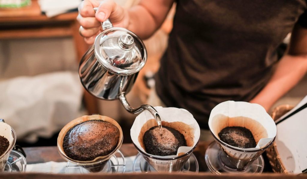 Drip brewing pouring water over roasted, ground coffee beans contained in a filter.