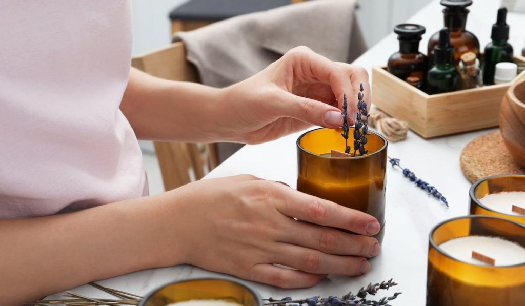 Woman decorating homemade candle with lavender flowers