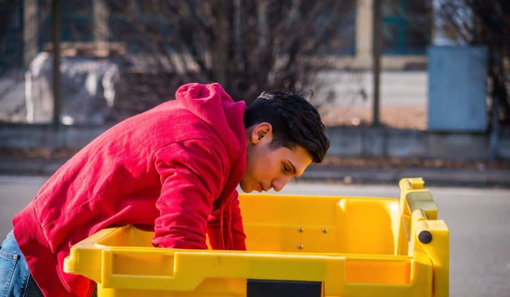 young man looking inside of a yellow dumpster