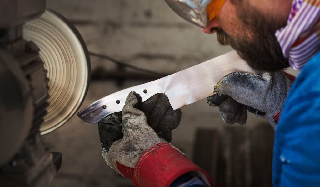 craftsman in a workshop holding a newly milled piece of knife with thick gloves