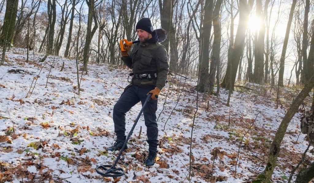 man with a metal detector and a shovel looking for treasure in snowy forest 