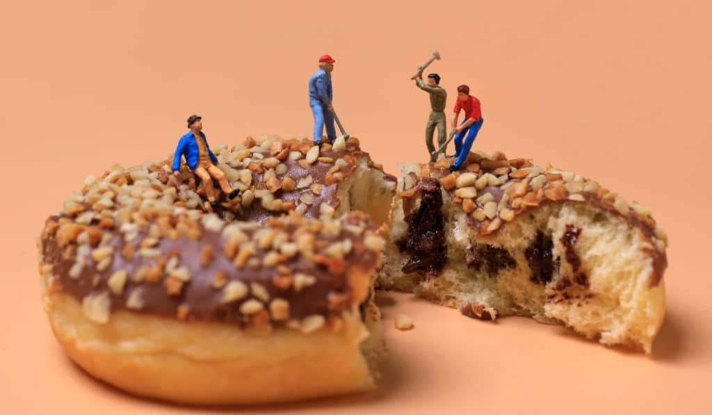 toy miniature workers work on big chocolate doughnut