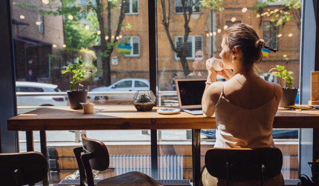 woman relaxing and drinking tea while sitting near the window in modern loft cafe bar