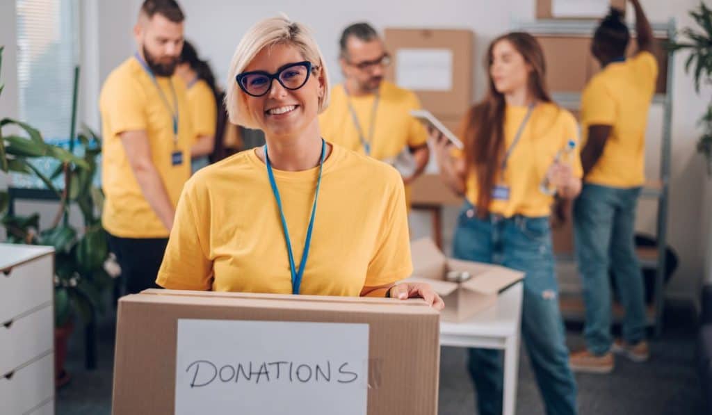 Group of volunteers on yellow shirt. Woman holding donation box with co-volunteers in the background
