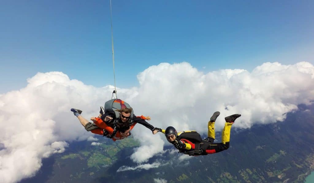 Portrait of tandem skydivers holding hands with female skydiver above clouds