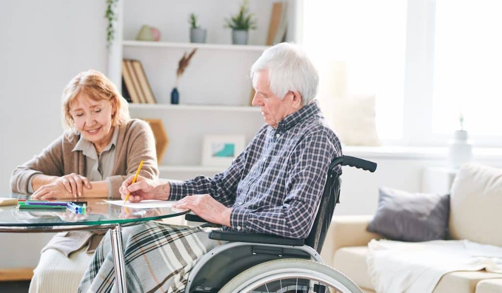 Senior man in wheelchair drawing on the table with his wife beside him