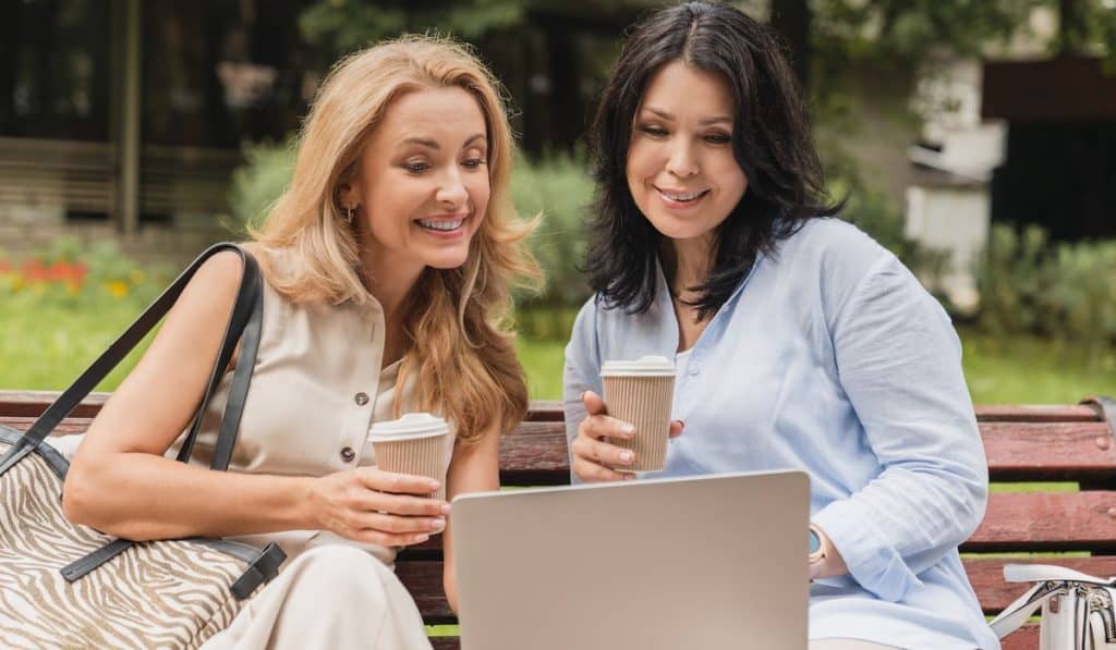 Two mature women discussing planning with their laptop and holding cup of coffee