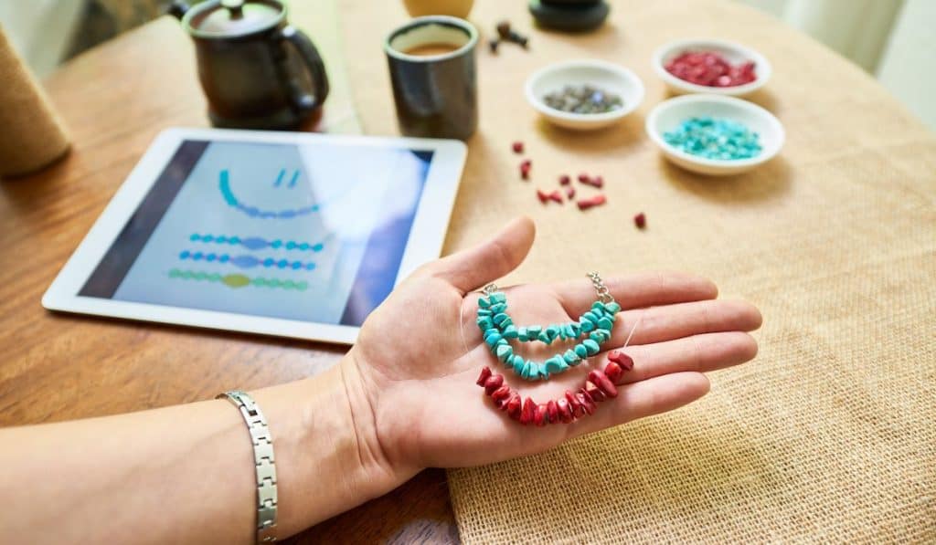 Woman's hand showing handmade jewelries mad by stone beads and tablet on the table